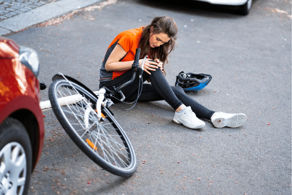 An image of a woman who has been involved in a bicycle accident, clutching her knee in pain and wincing, indicating discomfort or injury.