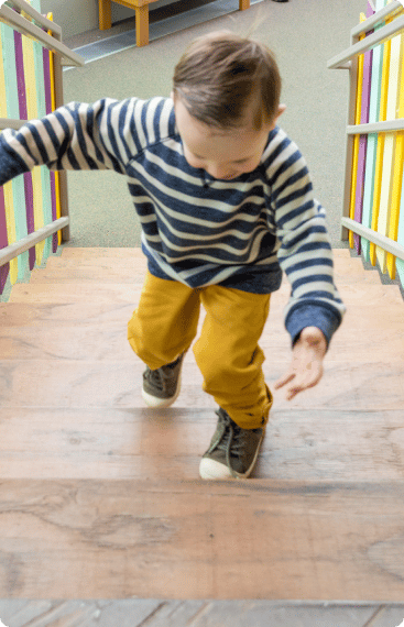 An image of a young child climbing a staircase with a happy expression on their face, indicating a sense of excitement or adventure.