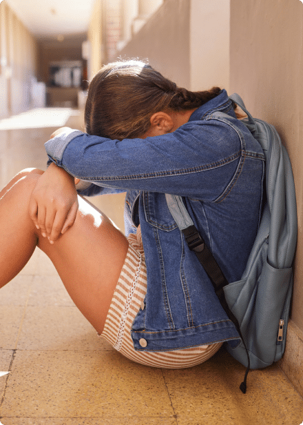 Person sitting on the ground and hunched over with their head down in their arms.