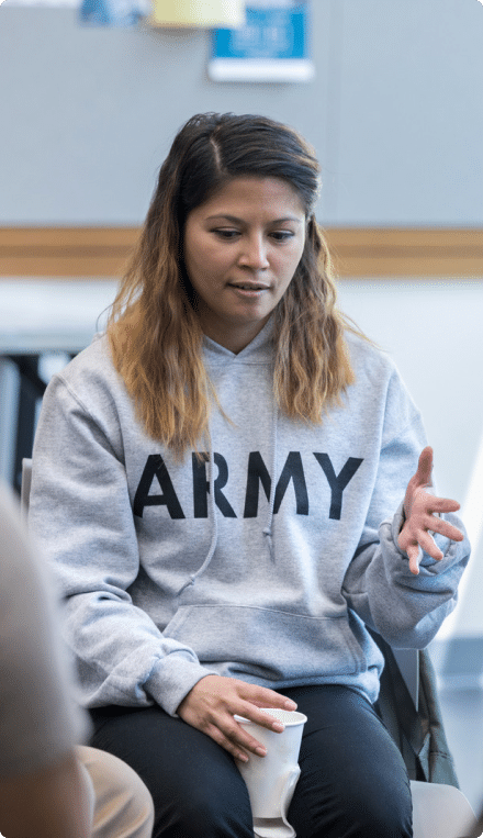 Woman wearing a grey hoodie that says "ARMY" sitting in chair and talking