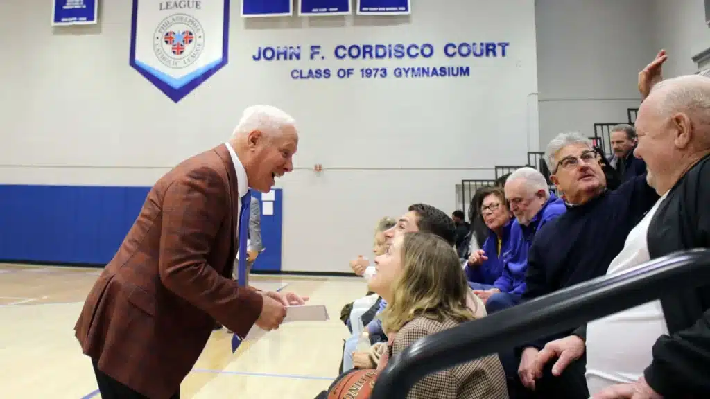 John Cordisco talking to people at a high school gymnasium
