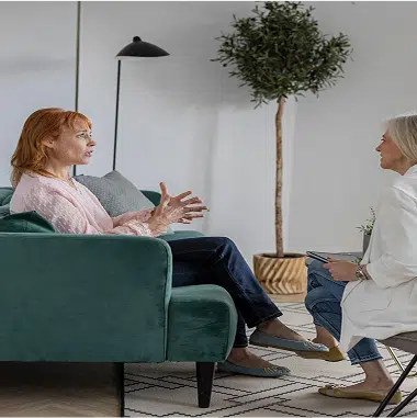 two women sitting down by couches and talking