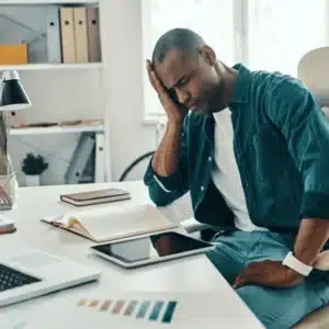 person holding head in hand while sitting at desk